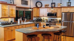 A modern kitchen with wooden cabinets, a stainless steel refrigerator, a built-in microwave, and a large island with bar stools.