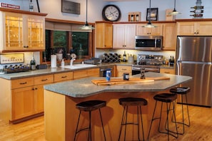 A modern kitchen with wooden cabinets, a stainless steel refrigerator, a built-in microwave, and a large island with bar stools.