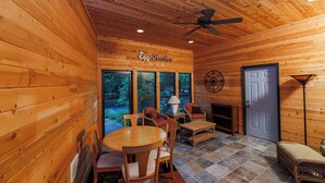 A wooden cabin interior with a dining table, chairs, a fireplace, and large windows.
