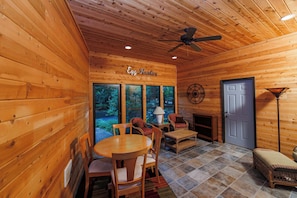 A wooden cabin interior with a dining table, chairs, a fireplace, and large windows.