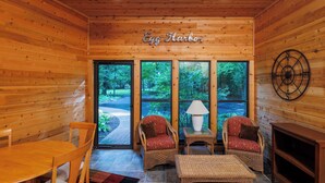 A wooden interior with a fireplace, two wicker chairs, a table, and a sign reading 'Egg Harbor'.