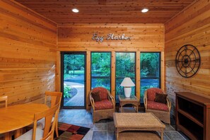A wooden interior with a fireplace, two wicker chairs, a table, and a sign reading 'Egg Harbor'.