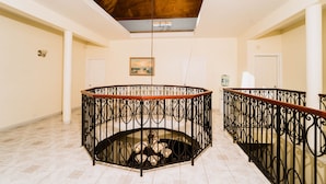 Un intérieur spacieux avec un escalier en colimaçon central, un plafond en bois et un tableau au mur.