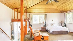 A bedroom with a wooden ceiling, a bed, a chair, a nightstand, and a window. - Tree House in Volcano Rainforest with a Hot Tub (Volcano)