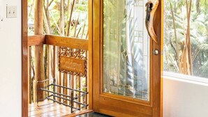 A wooden door with a glass panel and a handle, leading to a balcony with a metal railing and a bench. - Tree House in Volcano Rainforest with a Hot Tub (Volcano)