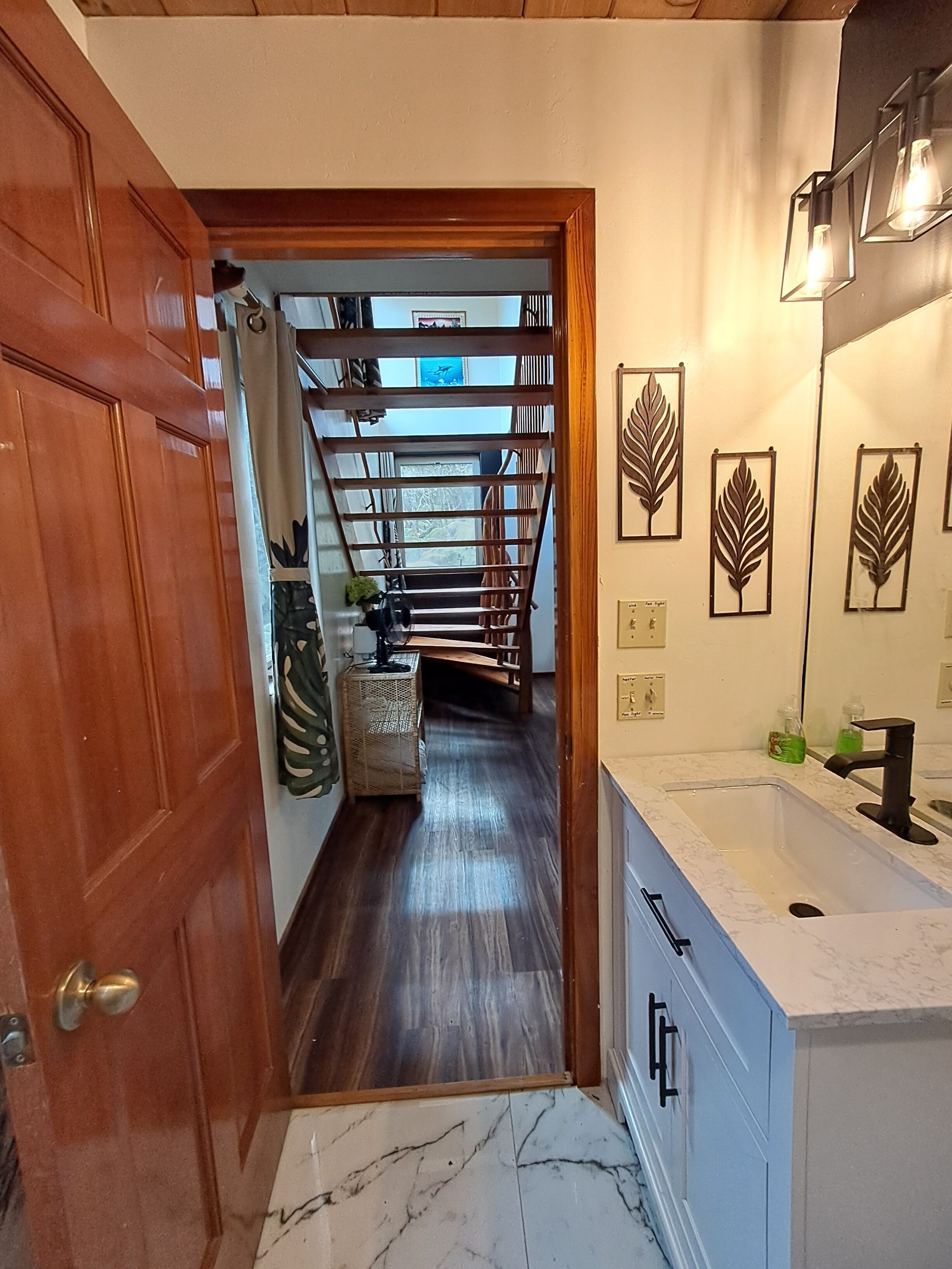 Un pasillo que conduce a un baño con puerta de madera, una escalera y suelo de mármol.