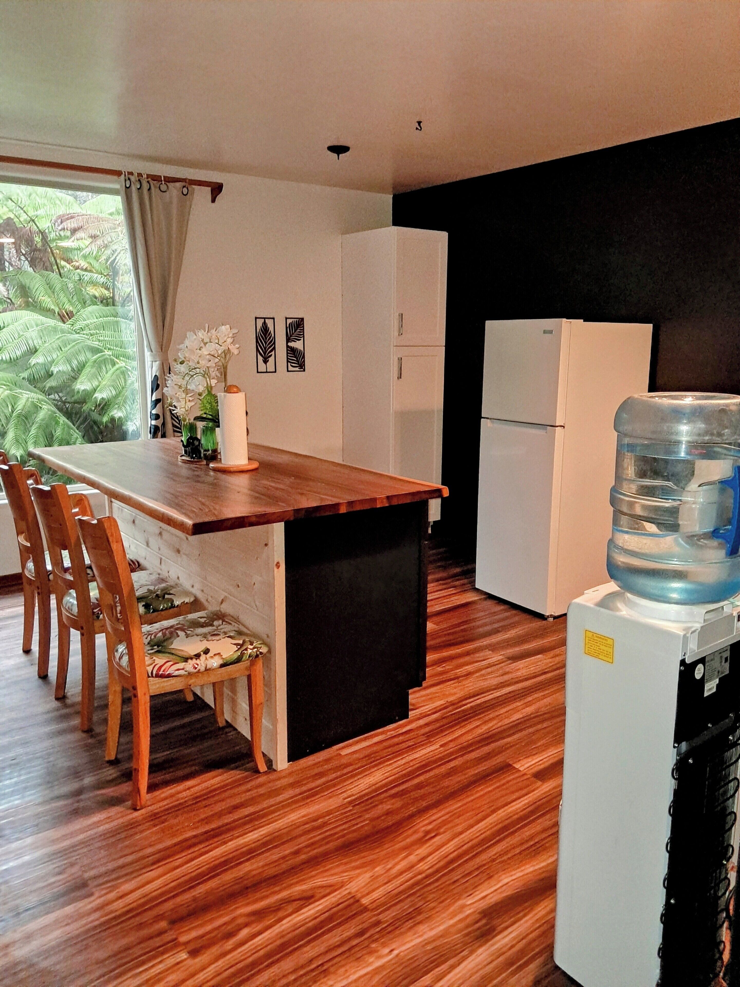 A compact kitchen with a wooden dining table, chairs, and a water dispenser.