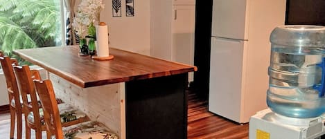 A compact kitchen with a wooden dining table, chairs, and a water dispenser.