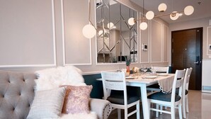 A modern dining area with a white table and chairs, a tufted sofa with fluffy pillows, and a chandelier with multiple light fixtures. - EEM Apartments Central (Ho Chi Minh City)
