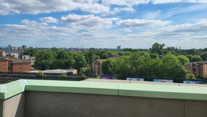 A cityscape with a mix of residential and commercial buildings, a clear sky with scattered clouds, and a green park area. - Garland Two Bedroom Apartment 1Min Walk to Station (London)