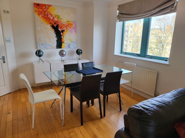 Ett modernt kontorsutrymme med ett glasbord, svarta stolar, ett vitt skrivbord och en färgstark, abstrakt målning på väggen.