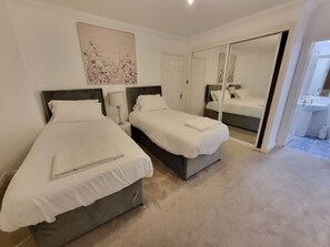 Ett hotellrum med två sängar, en stor spegel, en tavla och ett badrum som syns genom en öppen dörr.