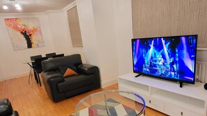 A living room with a black leather sofa, a glass coffee table, a flat-screen TV on a white stand, and a colorful rug. - Garland Two Bedroom Apartment 1Min Walk to Station (London)