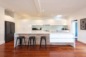 Cozinha moderna com armários brancos, uma ilha central com banquetas e uma geladeira de aço inoxidável.