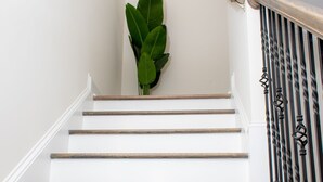 Una escalera con paredes blancas, escalones de madera y barandilla de metal negro.