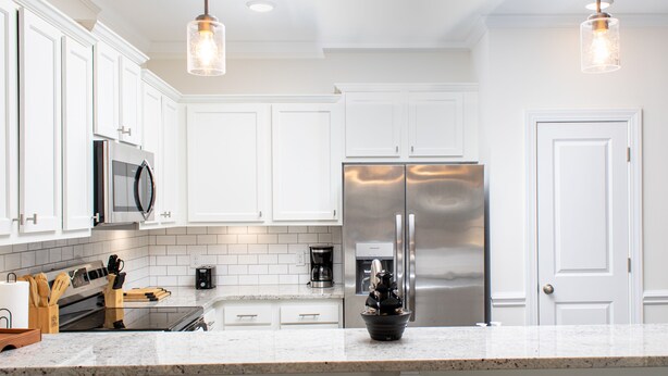 Una cocina moderna con armarios blancos, electrodomésticos de acero inoxidable e iluminación colgante.