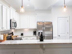 A modern kitchen with white cabinets, stainless steel appliances, and pendant lighting.