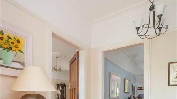 Un couloir doté d’un plancher en bois, d’une lampe, d’un tableau représentant des tournesols et d’une porte donnant sur une autre pièce.