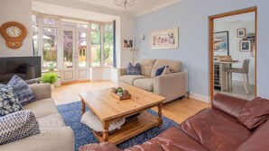 Un salon avec un canapé, une table basse et un téléviseur. Une grande fenêtre offre une vue sur un jardin.