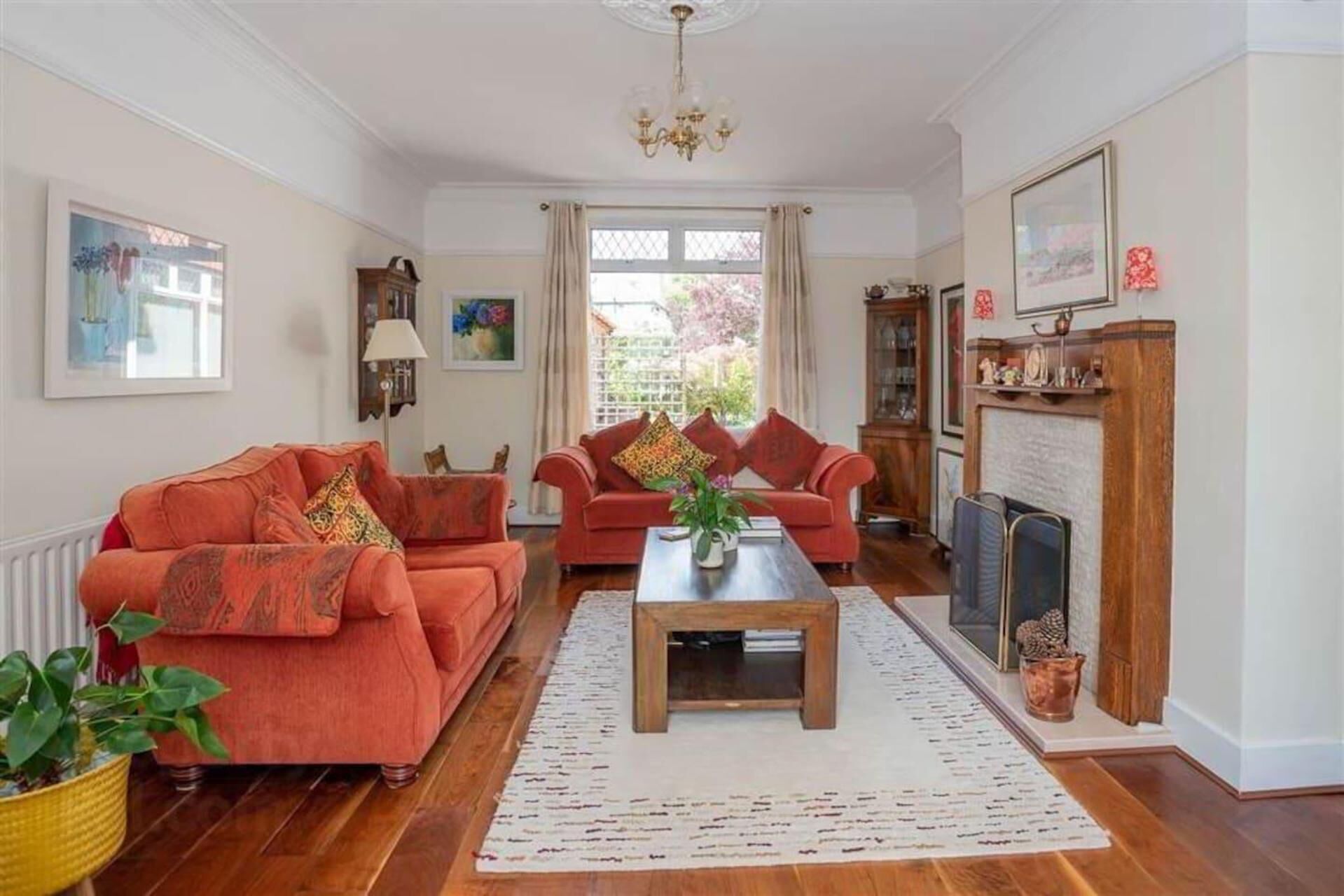 Ein Wohnzimmer mit zwei roten Sofas, einem Holztisch, einem Kamin und einem großen Fenster mit Vorhängen.