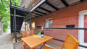 Une terrasse extérieure avec un mur en briques, un escalier en métal et une table avec des chaises.