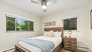 Une chambre à coucher avec un lit, des tables de chevet, un ventilateur de plafond et des fenêtres.