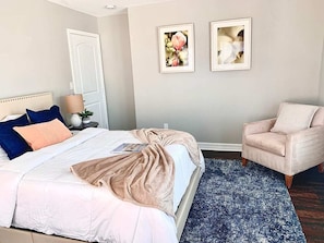 Une chambre à coucher comprenant un lit, une chaise, une table de chevet et deux tableaux encadrés accrochés au mur.