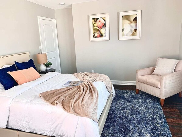 A bedroom with a bed, a chair, a nightstand, and two framed pictures on the wall.