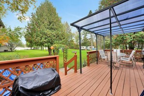 Eine Holzterrasse mit überdachtem Patio, Gartenmöbeln und einem Grill.