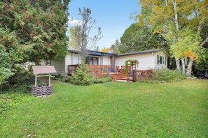Ein Bungalow mit Veranda, einer kleinen Terrasse und einem eingezäunten Garten.