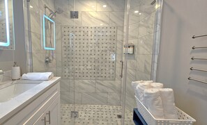 A modern bathroom with a glass-enclosed shower, a marble-tiled floor, a white sink, and a towel rack.
