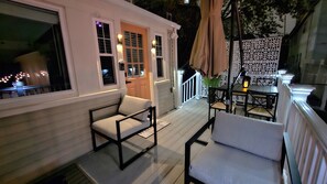 A covered outdoor seating area with two chairs and a table, a white door, and a white railing.