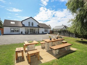 A large white house with a driveway and a patio area with wooden benches and tables. - Y Goedwig (Ty Croes)