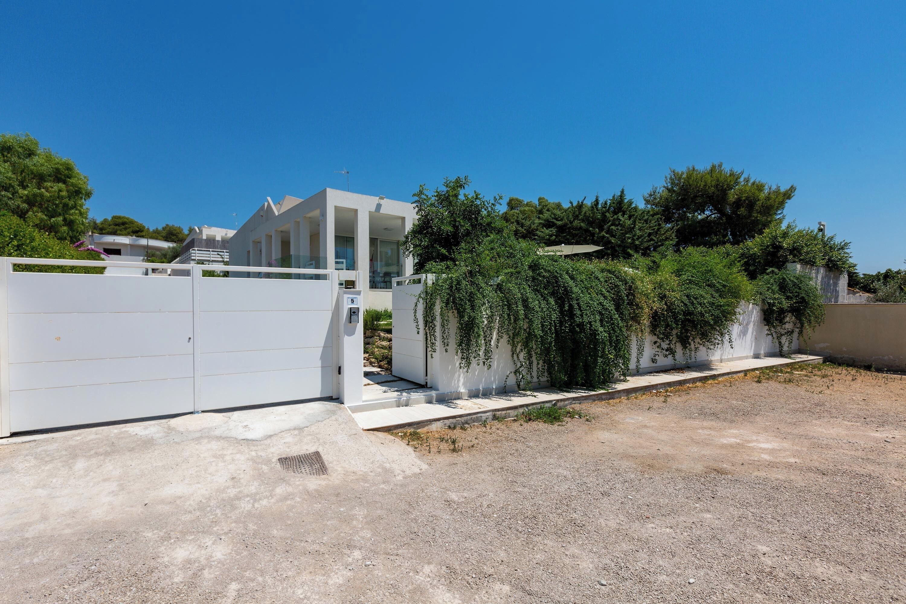 Una casa moderna con facciata bianca, vialetto recintato e un piccolo giardino con elemento d'acqua.