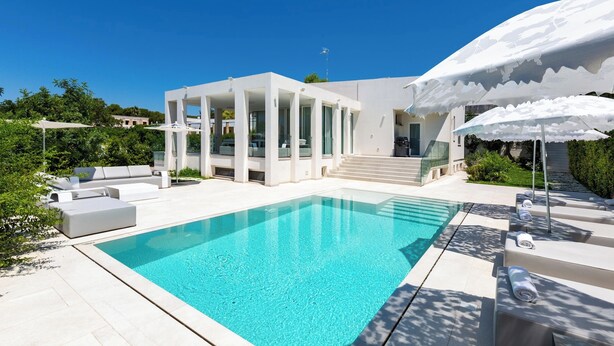 A modern poolside area with a clear pool, white outdoor furniture, and a covered seating area. - 2502 B&B Villa Eragea - Camere Standard by Barbarhouse (Matino)
