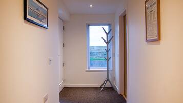 A hallway with a wooden floor, a window with a view of the countryside, and two framed pictures on the walls.