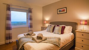 Un dormitorio con una cama grande, dos mesitas de noche con lámparas, una ventana con cortinas e imagen enmarcada en la pared.