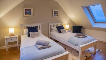 A cozy attic bedroom with two single beds, a skylight, and a small window.