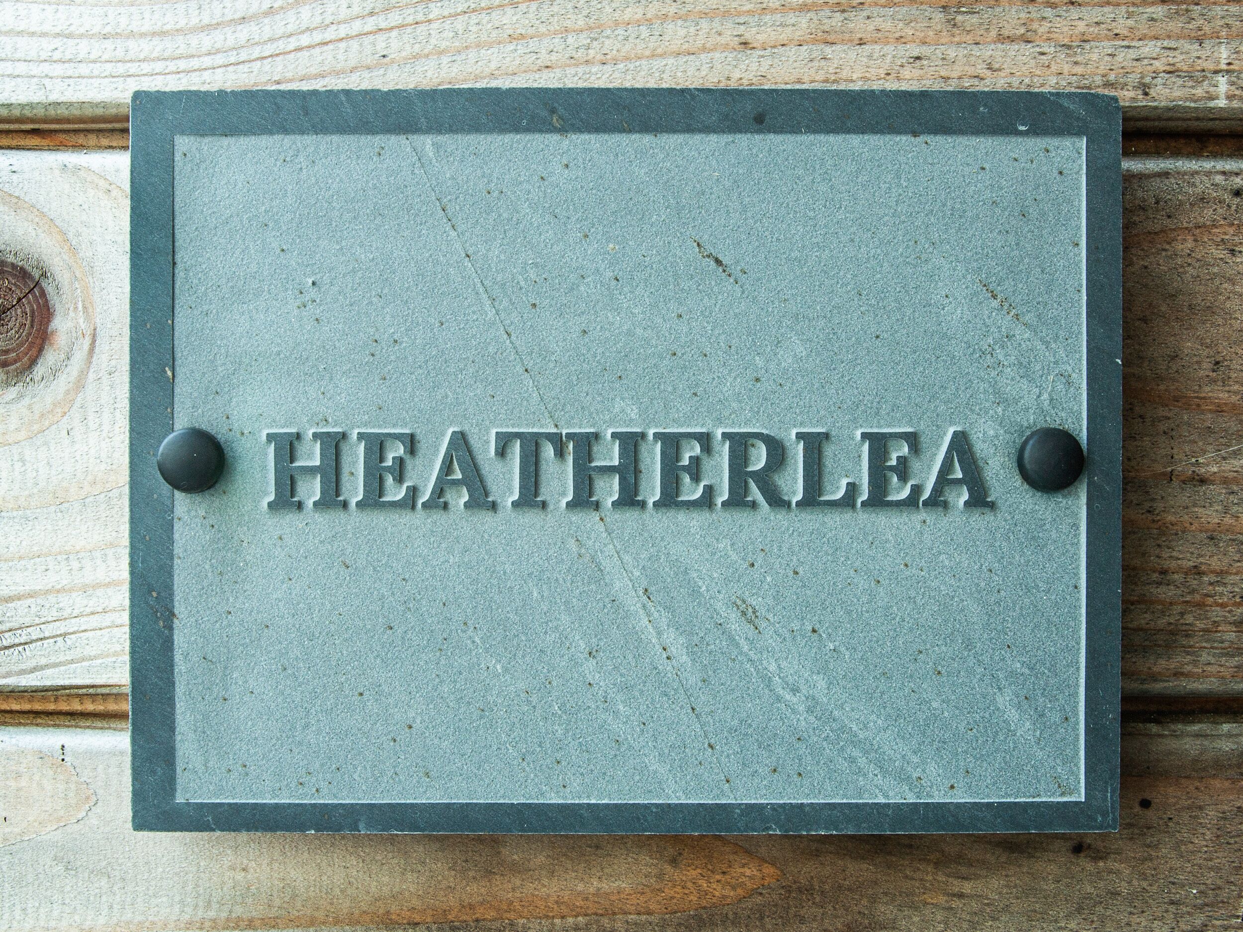 A metal plaque with the name "HEATHERLEA" mounted on a wooden surface.