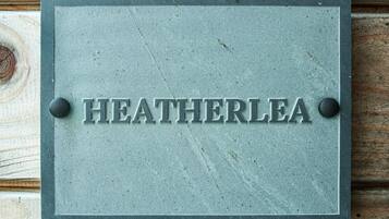 A metal plaque with the name "HEATHERLEA" mounted on a wooden surface.