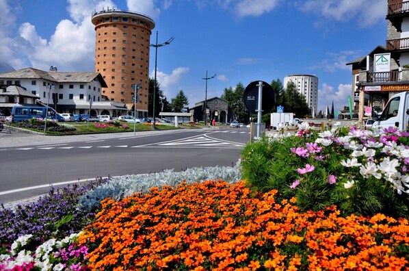 Una calle con un edificio circular, una cafetería y un jardín lleno de flores.