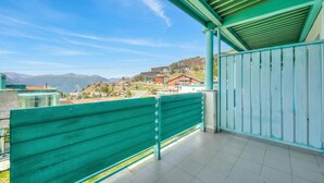 A balcony with a view of a hillside town, a green railing, and a clear sky. - Teleo 106 Ski In - Ski Out 50m, Sestriere, Italy (Sestriere)