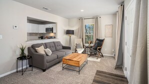 A modern living room with a grey sofa, a wooden coffee table, and a kitchen area in the background. - The Southern Sapphire: A Cozy Lake View Getaway (Granbury)