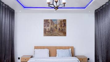 A modern bedroom with a large bed, two bedside tables, a painting on the wall, and a ceiling light fixture.