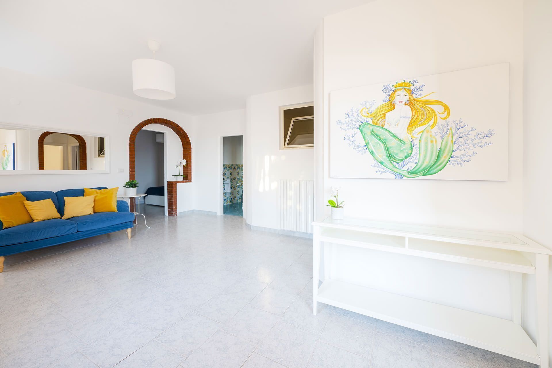 Uma sala de estar moderna com um sofá azul, mesa de apoio branca e uma grande pintura abstrata.