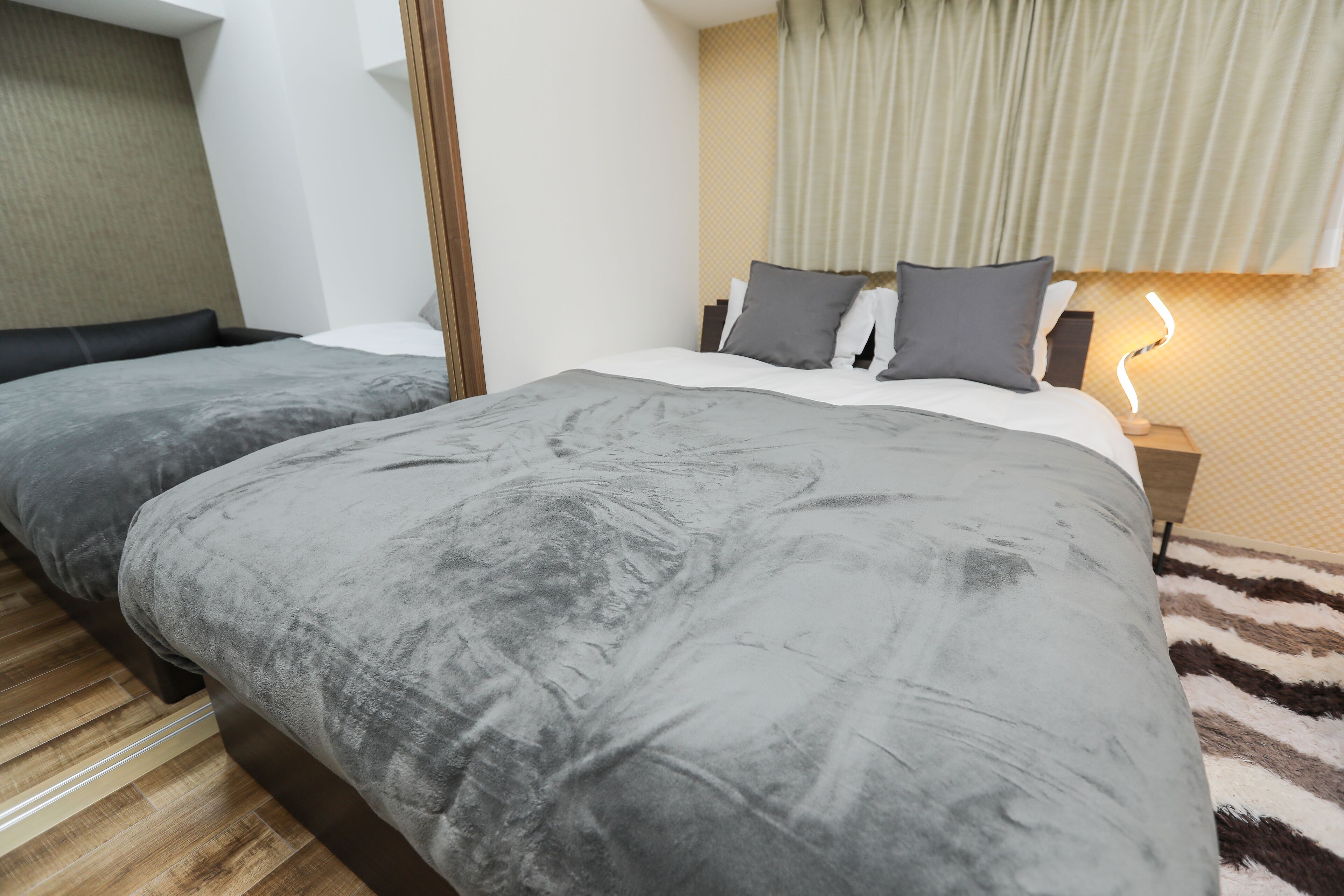 Una cama doble con ropa de cama gris, una mesita de noche con lámpara y una alfombra estampada.