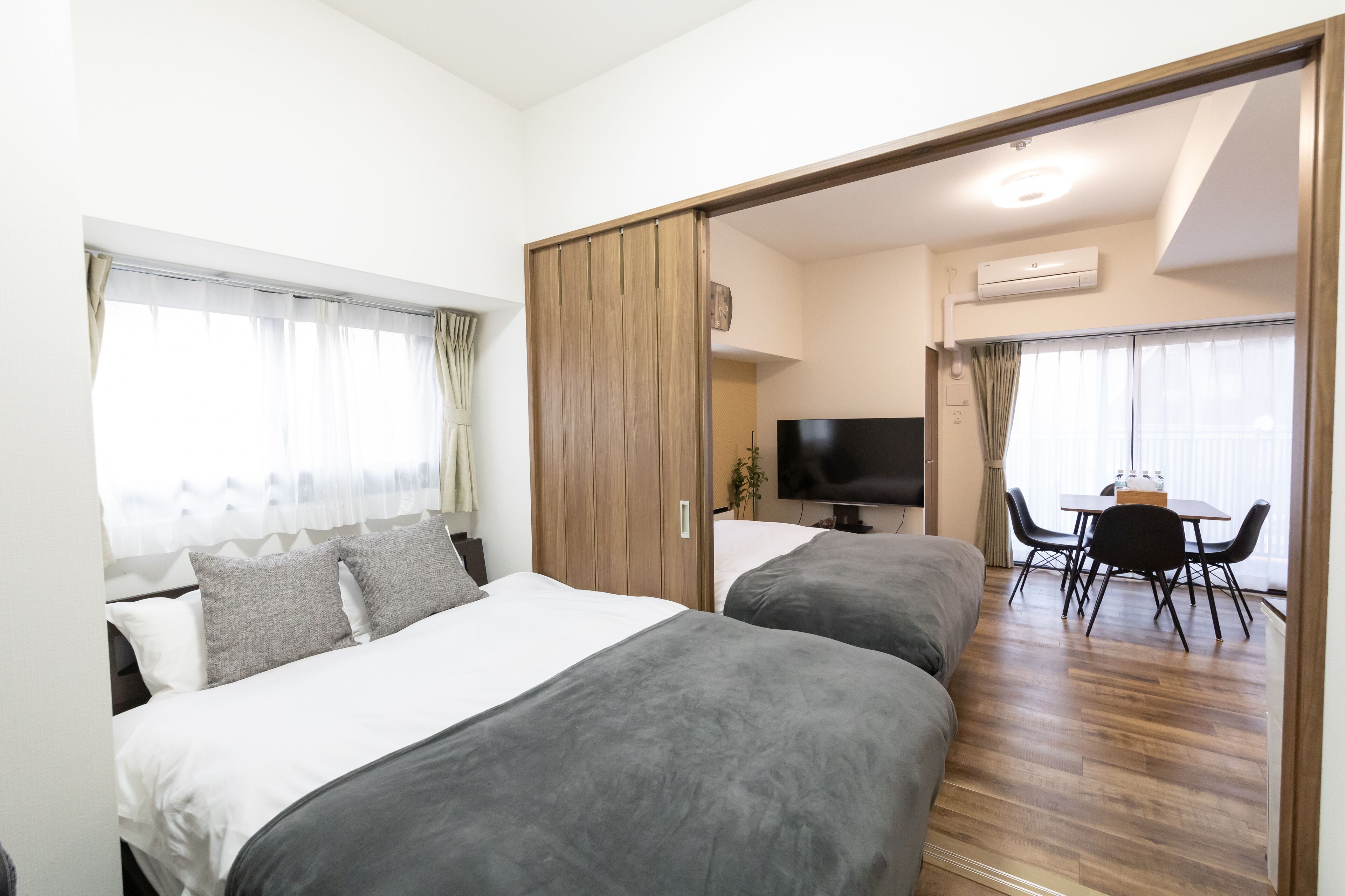 Une chambre d’hôtel avec deux lits, une télévision, une table à manger avec des chaises et un placard à portes coulissantes.