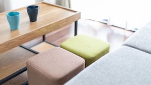 Un soggiorno moderno con un tavolino in legno, due tazze e tre poggiapiedi dai colori diversi.