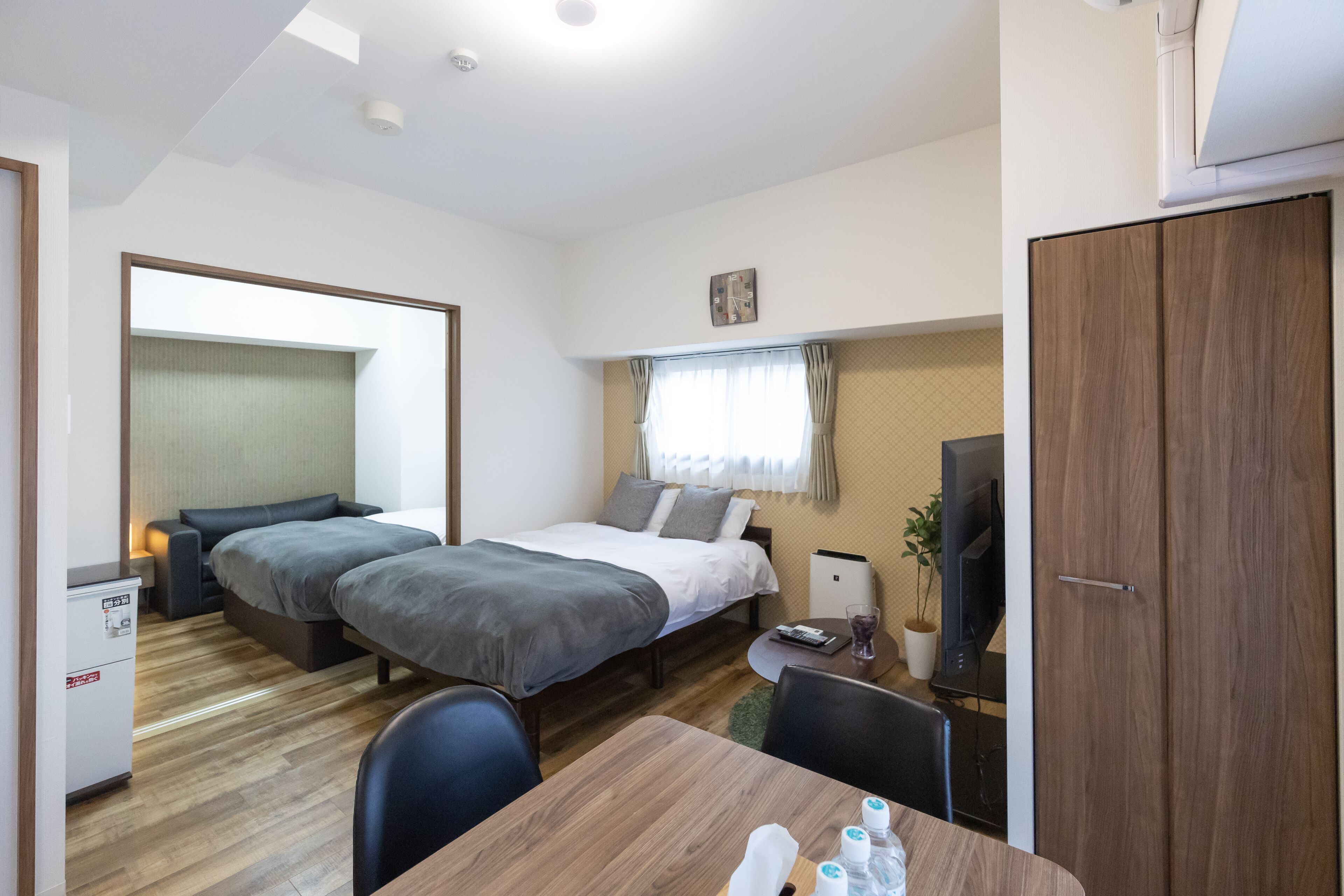Quarto de hotel compacto com duas camas de solteiro, uma secretária pequena, uma cadeira, televisão e guarda-roupa.