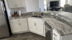 A modern kitchen with white cabinets, a stainless steel refrigerator, and a granite countertop.